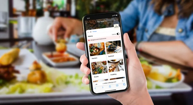 Hand holding a phone showing a food menu above a plated meal at a table