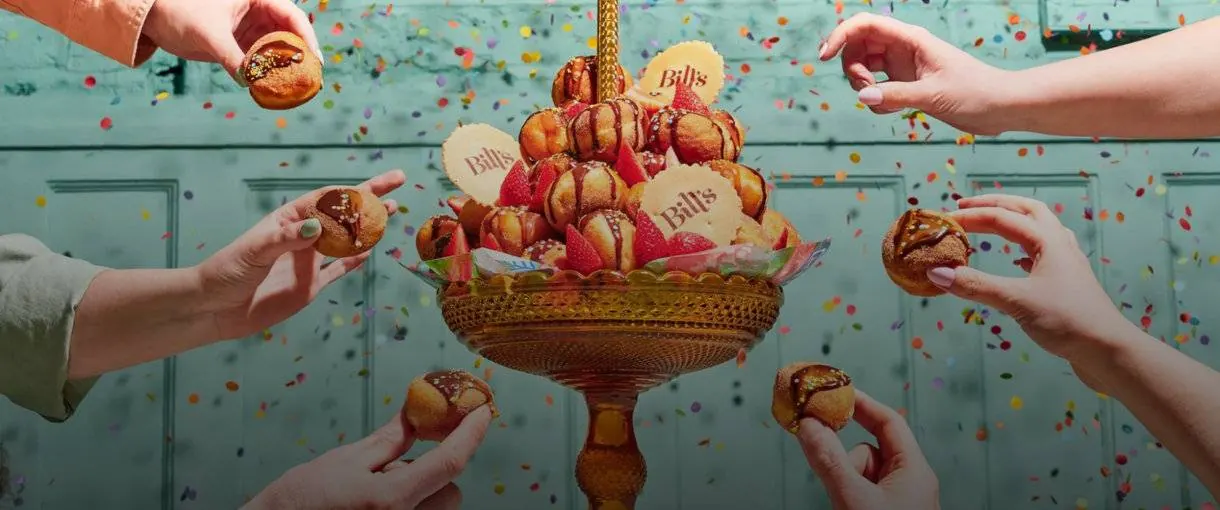 Hands reaching for macarons stacked in a tiered stand against a teal wall