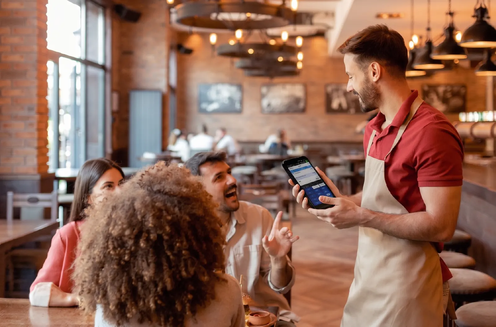 Waiter holding a handheld terminal while talking with diners in a restaurant