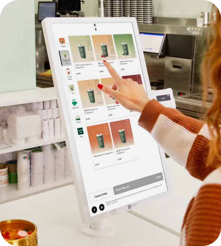 Customer touching a menu on a self-ordering kiosk touchscreen at a counter