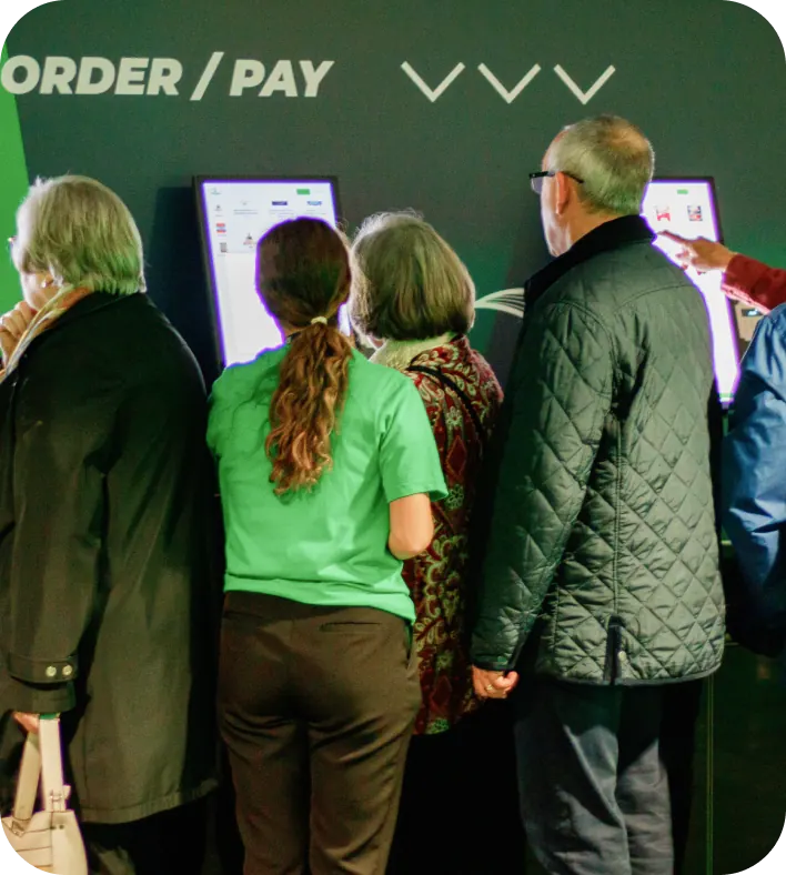 Group of people ordering at a bank of kiosks under an order and pay sign